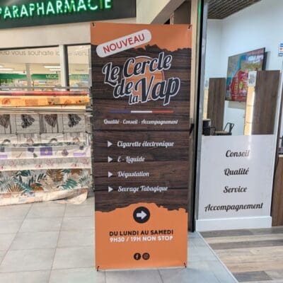 Kakemono vertical du magasin Le Cercle de la Vap installé dans une galerie commerciale, aux tons orange et bois, listant les services et horaires.