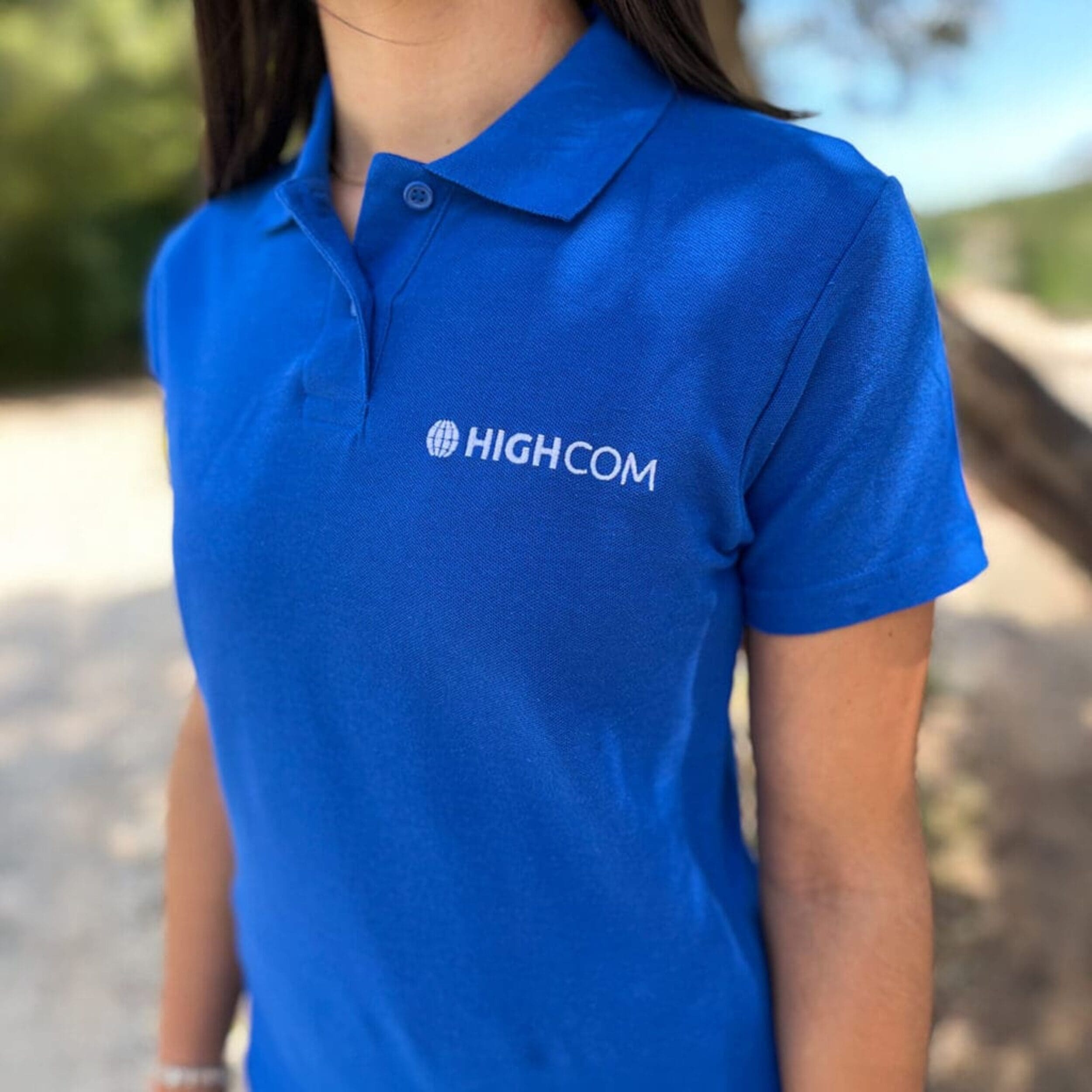 Personne portant un polo bleu avec le logo "HIGHCOM" brodé en blanc sur la poitrine.
